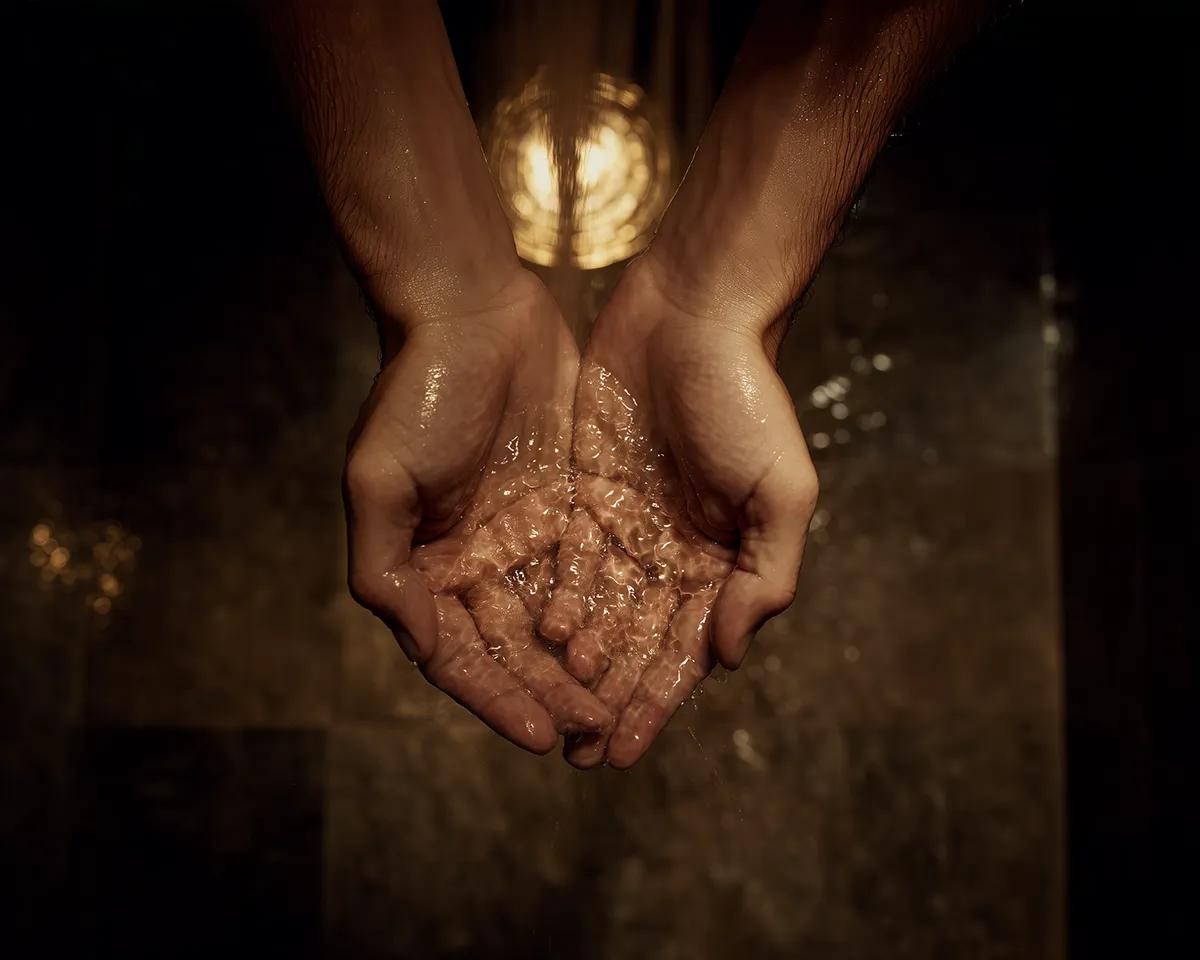 Männliche Hände halten Wasser unter der Dusche – warmes Licht, dunkles Badezimmer