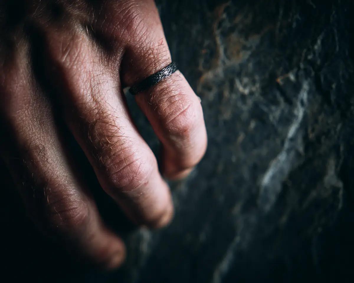 Männliche Hand halb geschlossen mit schwarzem strukturiertem Ring am Mittelfinger – Nahaufnahme auf dunklem Stein, dramatisches Seitenlicht
